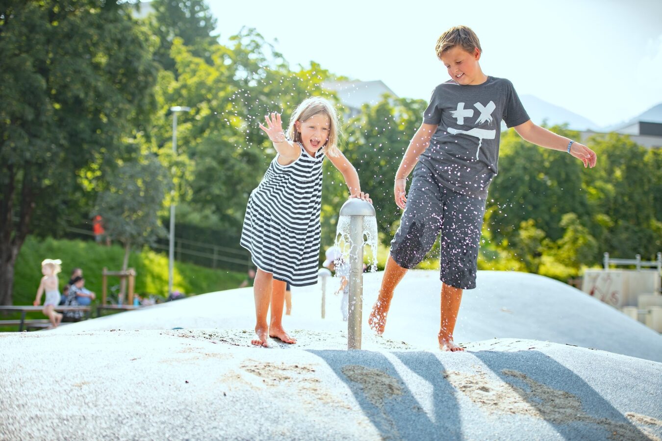 Junge und Mädchen spielen mit Wasser am Brunnen am Spielplatz